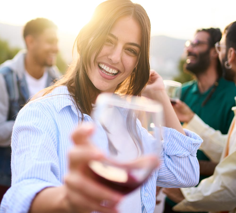 A smiling woman raising a glass of red wine with friends at a Fredericksburg vineyard at sunset